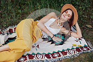 A woman in eco-friendly clothing in a hippie look is lying on a colored plaid smiling and looking at an autumn sunset in