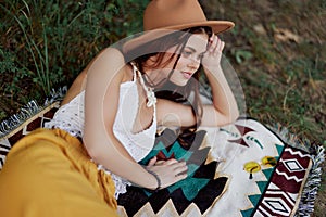 A woman in eco-friendly clothing in a hippie look is lying on a colored plaid smiling and looking at an autumn sunset in