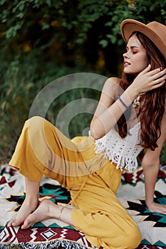 A woman in eco-friendly clothing in a hippie look is lying on a colored plaid smiling and looking at an autumn sunset in