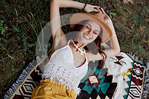 A woman in eco-friendly clothing in a hippie look is lying on a colored plaid smiling and looking at an autumn sunset in