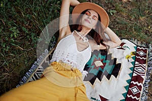 A woman in eco-friendly clothing in a hippie look is lying on a colored plaid smiling and looking at an autumn sunset in