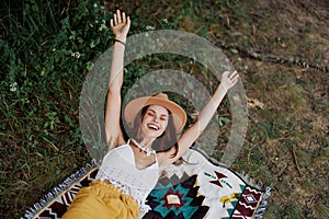 A woman in eco-friendly clothing in a hippie look is lying on a colored plaid smiling and looking at an autumn sunset in