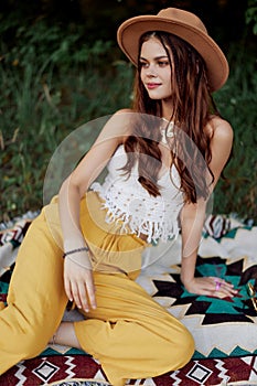 A woman in eco-friendly clothing in a hippie look is lying on a colored plaid smiling and looking at an autumn sunset in