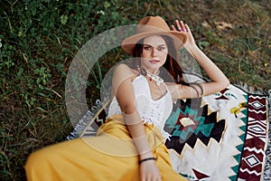 A woman in eco-friendly clothing in a hippie look is lying on a colored plaid smiling and looking at an autumn sunset in