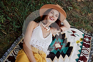 A woman in eco-friendly clothing in a hippie look is lying on a colored plaid smiling and looking at an autumn sunset in