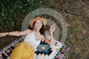 A woman in eco-friendly clothing in a hippie look is lying on a colored plaid smiling and looking at an autumn sunset in