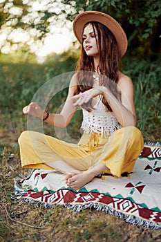 Woman in ecological clothing in a hippie look sits on a colored plaid meditating in the lotus position smiling and