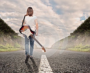 Woman with an electric guitar walking on a road