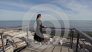 Woman with elegant dress moved by the wind watching the sea on the horizon