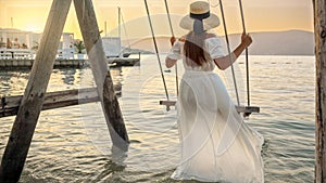 Woman in an elegant long dress enjoys a sway under the setting sun. Tourism, the tranquility of summertime, freedom, and