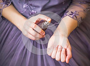 Woman in elegant purple dress applying perfume on her wrist closeup