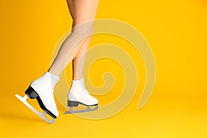 Woman in elegant white ice skates on yellow background, closeup of legs. Space for text