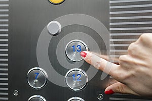 Woman in elevator or lift is pressing button to get into right floor only hand to be seen - close-up. 13 th floor