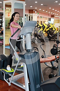 Woman with elliptical cross trainer at gym. Muscular, interior