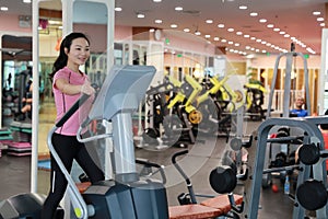 Woman with elliptical cross trainer at gym. Muscular, interior