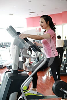 Woman with elliptical cross trainer at gym. Muscular, interior