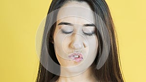 Woman with emotion of patience bites lip on yellow background. Slowly