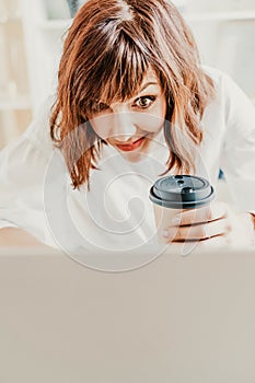 Woman emotions communication at the computer. The brunette holds a glass of coffee and looks in surprise at her laptop