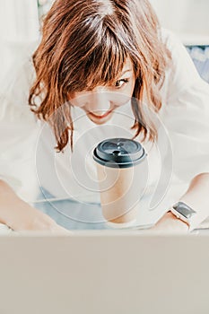 Woman emotions communication at the computer. The brunette holds a glass of coffee and looks in surprise at her laptop