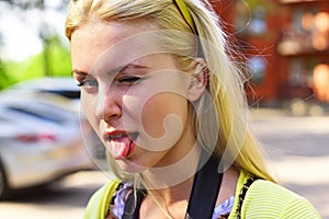 Woman emotions face. Girl shows tongue outdoor.