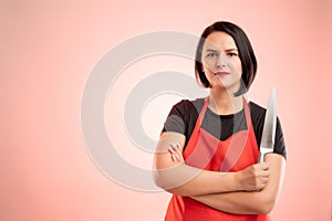 Woman employed at supermarket with red apron and black t-shirt she confidently holds a knife in her hand