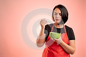 Woman employed at supermarket with red apron and black t-shirt cool the soup, hold the bowl in her hand