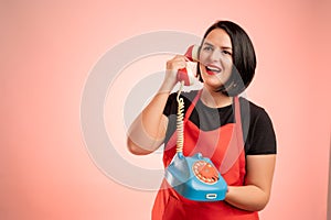 Woman employed at supermarket with red apron and black t-shirt happy talking on an old phone