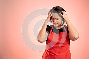 Woman employed at supermarket with red apron and black t-shirt has headache