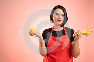 Woman employed at supermarket with red apron and black t-shirt hold a lemon and a lemon juicer in her hand