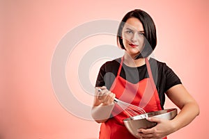 Woman employed at supermarket with red apron and black t-shirt hold metal bowl and wire in her hand