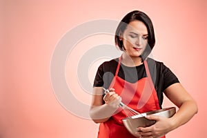 Woman employed at supermarket with red apron and black t-shirt hold metal bowl and wire in her hand