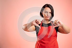 Woman employed at supermarket with red apron and black t-shirt showing double dislike