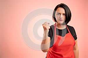 Woman employed at supermarket with red apron and black t-shirt showing fist