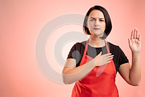 Woman employed at supermarket with red apron and black t-shirt showing oath