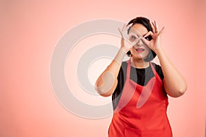 Woman employed at supermarket with red apron and black t-shirt showing Ok gestures with both hands