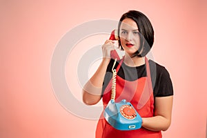 Woman employed at supermarket with red apron and black t-shirt talking on an old phone