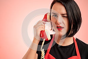 Woman employed at supermarket with red apron and black t-shirt talking on an old recever