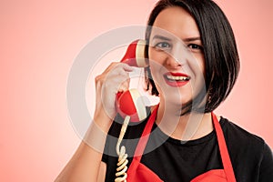 Woman employed at supermarket with red apron and black t-shirt talking on an old recever smiling at camera