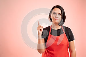 Woman employed at supermarket with red apron and black t-shirt thinking of an idea