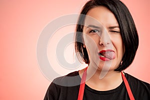 Woman employed at supermarket with red apron and black t-shirt winking one eye