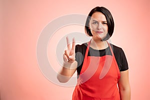 Woman employed at supermarket with red apron showing victory