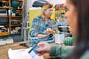 Woman employee checking on computer price of jeans and customer holding credit card to pay purchase