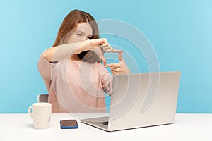 Woman employee, designer or photographer, making photo frame with hands and focusing at laptop screen