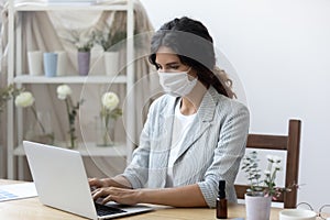 Woman employee in medical mask work on laptop in office