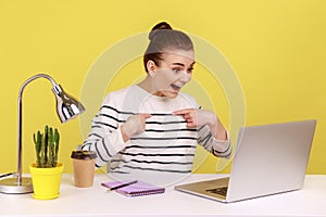 Woman employee pointing herself and smiling proudly, boasting promotion, sitting at workplace.