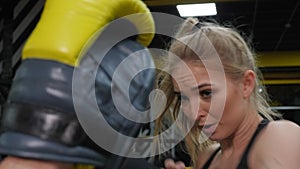 A woman is engaged in boxing in the gym with a trainer, she practices punches.