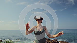 Woman engages in VR experience by seaside, interacts with virtual interface, games, browses metaverse. Coastscape