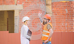 Woman engineer and bearded brutal builder discuss construction progress. Construction project management. Building