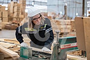 woman engineer carpenter wearing safety uniform and hard hat working on wood cutting electric machines at workshop manufacturing