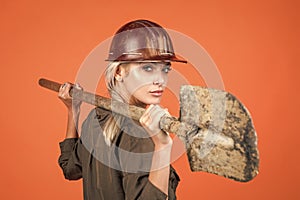 woman engineer in protective helmet and boilersuit hold shovel on orange background, engineering